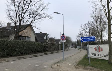 Foto van een straat met links een woning en rechts een school.