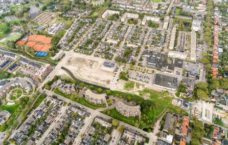 Luchtfoto van het centrum van Badhoevedorp. Met 3 half ovale appartementengebouwen en platte daken van winkels. Daaromheen woonwijken. Ook is er ruimte vrij in het  midden waar gebouwd gaat worden.