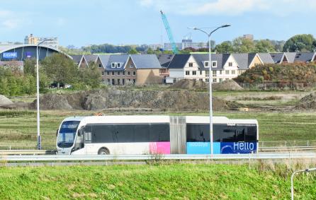 Witte bus rijdt op een straat. Met op de achtergrond Badhoevedorp.
