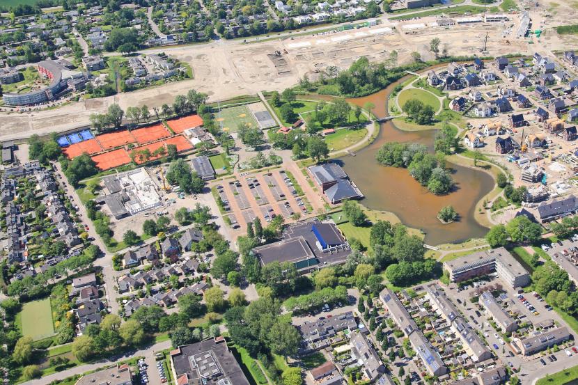 Luchtfoto met een park met water, bestaande huizen en een bouwplaats met nieuwbouwwoningen