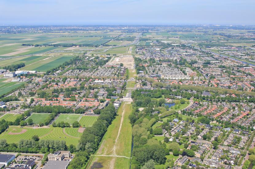 Luchtfoto van een dorp met woningen en in het midden een brede strook gras. Hier was vroeger de snelweg A9.