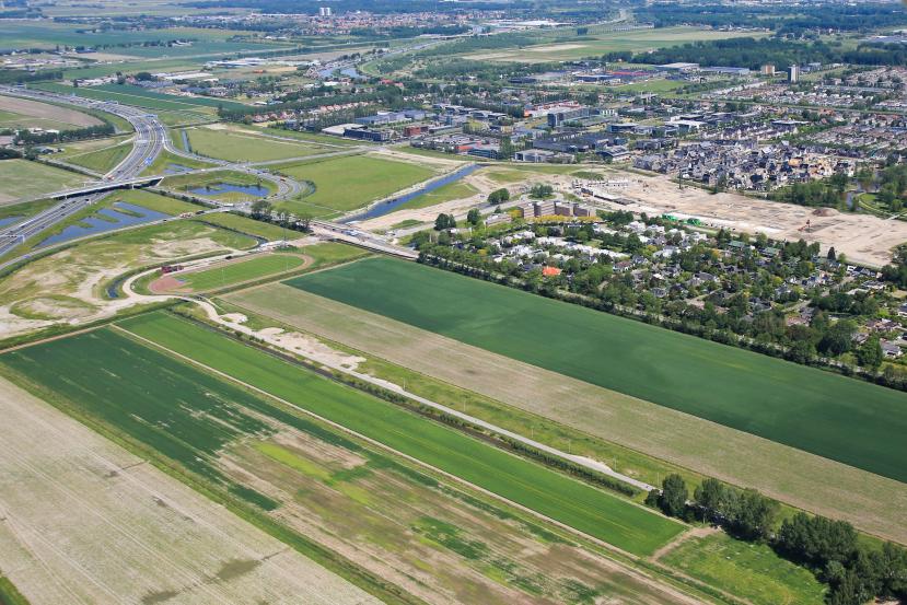 Luchtfoto van groene weilanden, een atletiekbaan en een dorp.