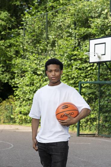 Op de foto staat Kenneth op een sportveldje met een basketbal in zijn hand.