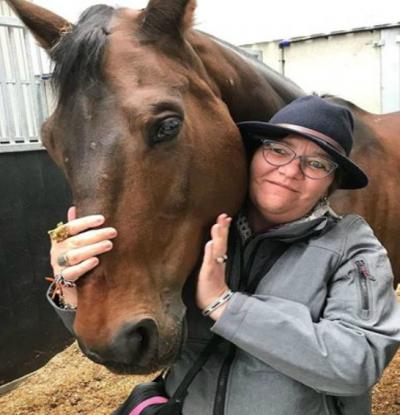 Caroline Schaad poseert met een paard op een manege waar ze mensen met een beperking helpt bij het paardrijden.